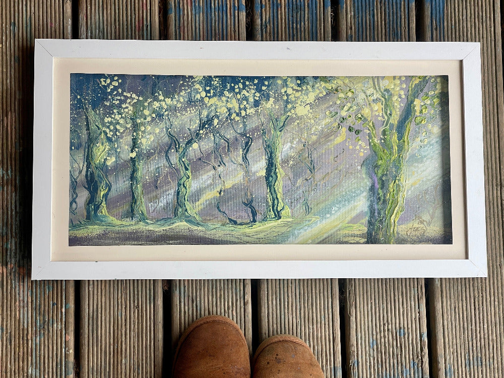 Framed artwork of a forest scene on a wooden surface