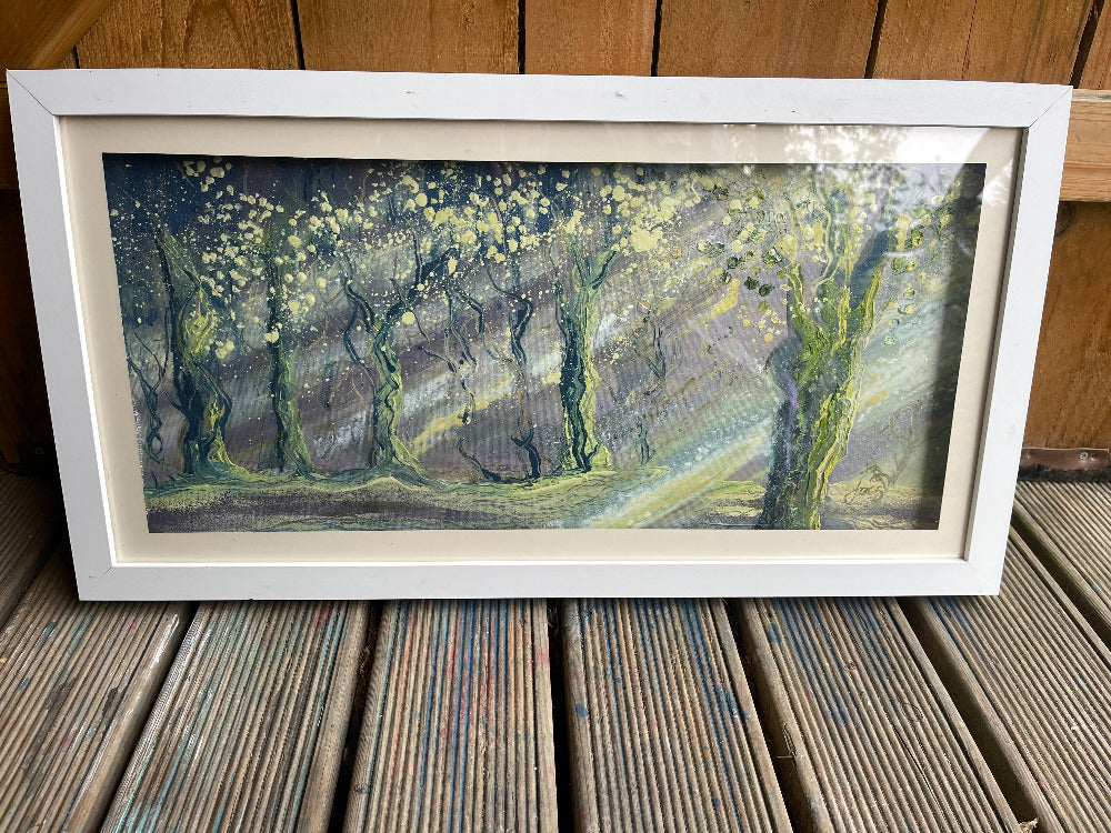 Framed painting of a forest scene on a wooden surface