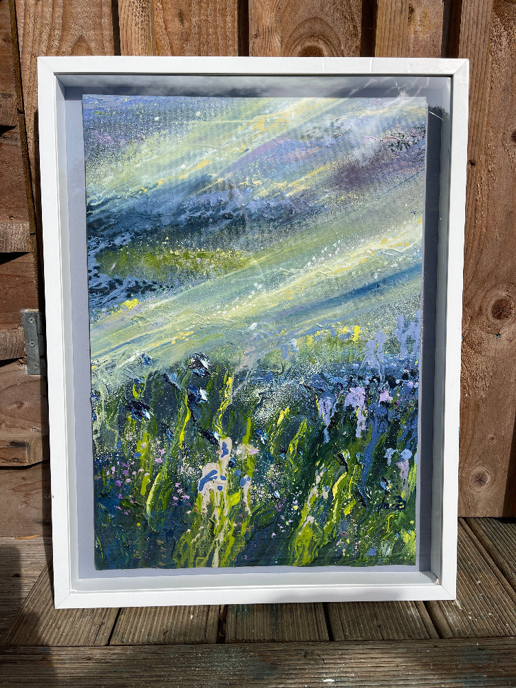 Framed abstract painting with green and blue hues on a wooden surface