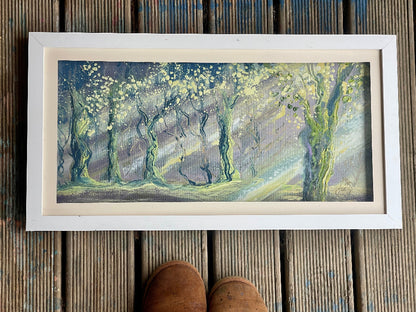 Framed artwork of a forest scene on a wooden surface
